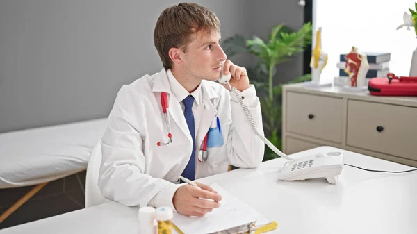 年轻的高加索男医生在诊所的文件上讲电话写作 — 图库照片