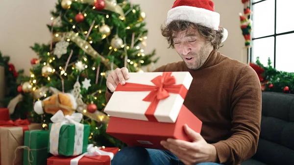 若いヒスパニックの男は自宅でソファーに座ってクリスマスの贈り物を荷を解く — ストック写真