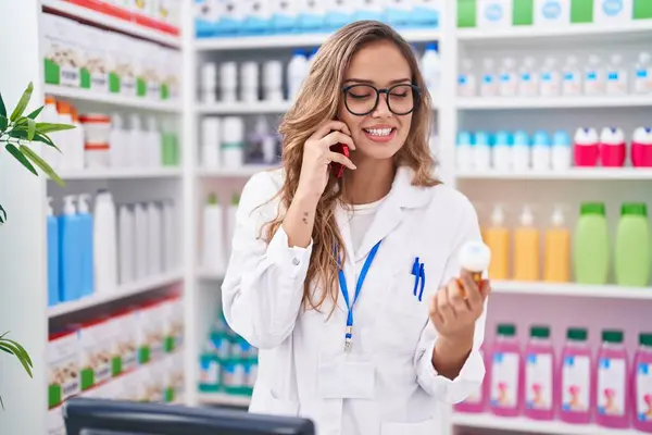 Jovem Bela Mulher Hispânica Farmacêutico Segurando Pílulas Garrafa Falando Smartphone — Fotografia de Stock