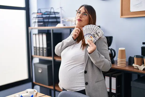 怀孕的女人手里拿着钱在办公室里认真地 手托着下巴地思考着问题 思考着令人困惑的想法 — 图库照片