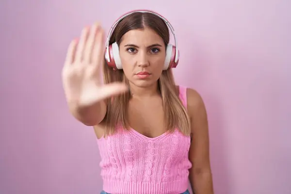 年轻的金发女人在用耳机听音乐时 不要再用手拍掌唱歌了 用消极而严肃的手势警告人 — 图库照片