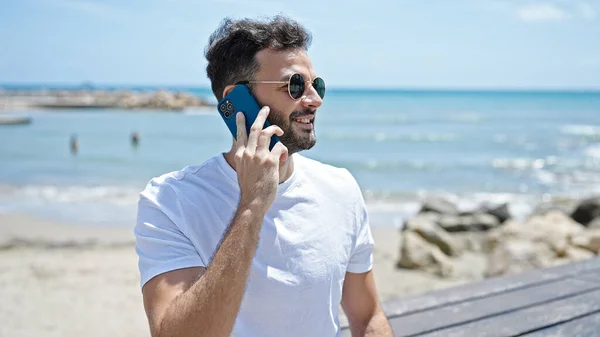 Joven Hombre Hispano Sonriendo Confiado Hablando Teléfono Inteligente Playa —  Fotos de Stock