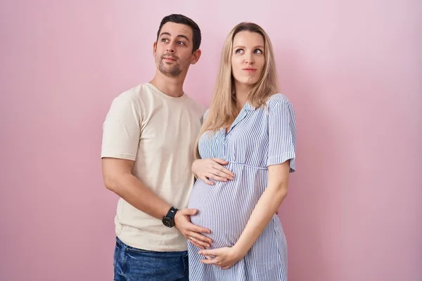 若いカップルは ピンクの背景の上に立っている赤ん坊を期待し 横を見つめ 考えを遠ざける — ストック写真