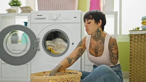 Hispanic woman with amputee arm washing clothes sitting on floor at laundry room