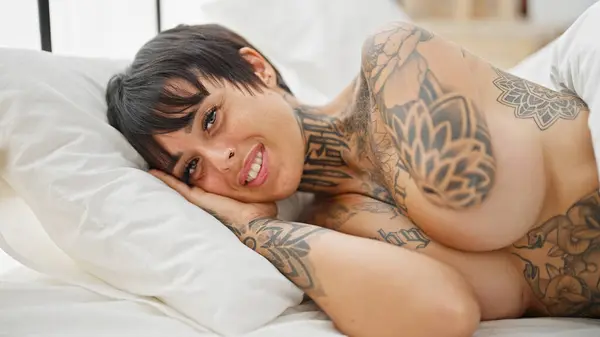 Hispanic woman with amputee arm lying on bed shirtless smiling at bedroom