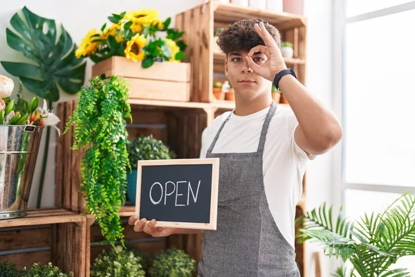 Çiçekçide çalışan İspanyol bir genç elinde açık tabela, gülümsüyor. Mutluluktan gülümsüyor. 