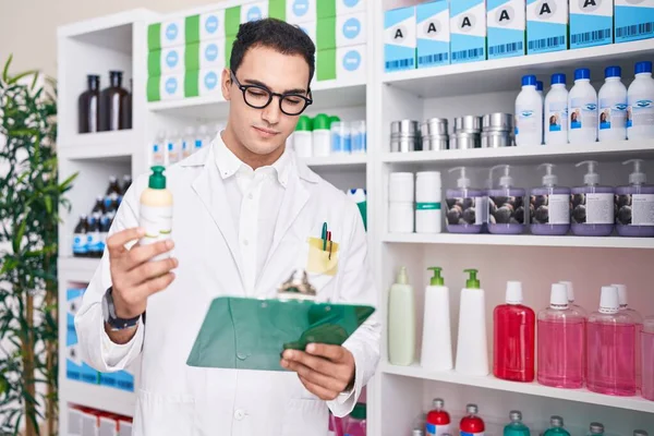 Young Hispanic Man Pharmacist Reading Document Holding Shampoo Pharmacy — Stockfoto