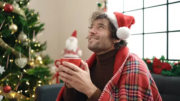 自宅でクリスマスツリーでソファーに座ってコーヒーを飲む若いヒスパニック男性 — ストック写真