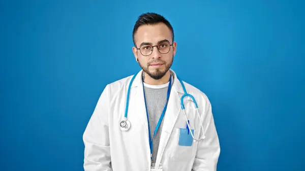 西班牙裔男子医生 严肃地站在孤立的蓝色背景下 — 图库照片