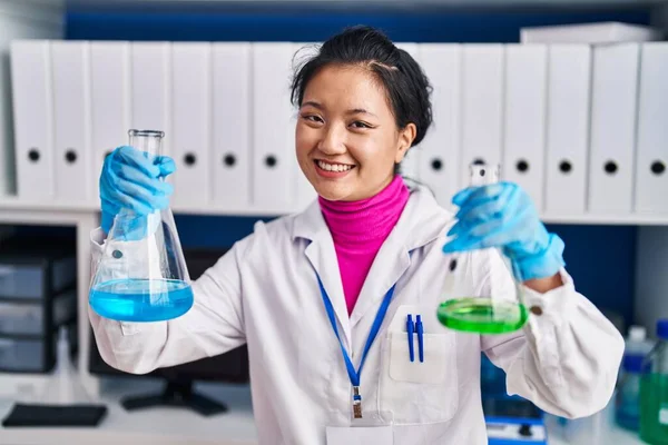 Young chinese woman scientist smiling confident holding test tubes at laboratory