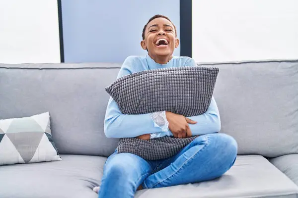 Mujer Afroamericana Sentada Sofá Casa Abrazando Almohada Sonriendo Riendo Voz —  Fotos de Stock