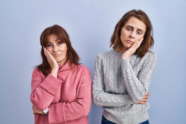 stock image Mother and daughter standing over blue background thinking looking tired and bored with depression problems with crossed arms. 