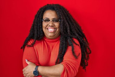 Ayrıca kırmızı arka planda dikilen boyunda İspanyol bir kadın kollarını kavuşturup kameraya bakarken gülümsüyor. pozitif kişi. 