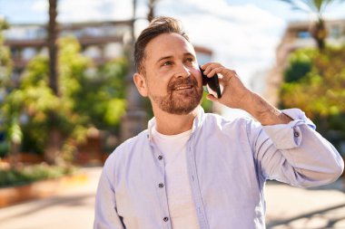 Genç beyaz adam gülümsüyor. Parktaki akıllı telefondan konuşuyor.