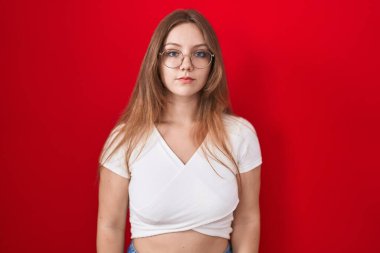 Kırmızı arka planda duran beyaz bir kadın yüzünde ciddi bir ifadeyle rahatlamış. Basit ve doğal bir şekilde kameraya bakıyorsun.. 