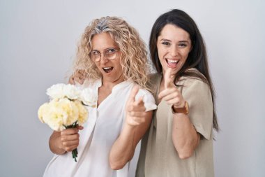 Anne ve kızı ellerinde buket beyaz çiçeklerle mutlu ve komik yüzlü parmaklarını kameraya doğrultuyorlar. iyi enerji ve titreşimler. 
