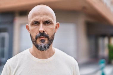 Sokakta ciddi bir ifadeyle duran genç kel adam.