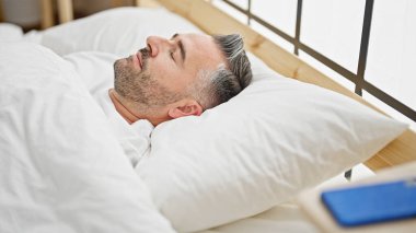 Gri saçlı adam yatakta uzanıyor, yatak odasında uyuyor.