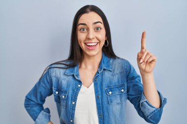 Mavi arka planda duran İspanyol kadın başarılı bir fikirle işaret ediyor. Heyecanlı ve mutlu. Bir numara.. 