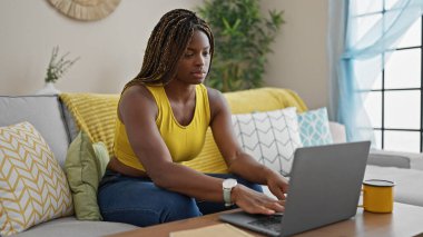 African american woman using laptop sitting on sofa at home