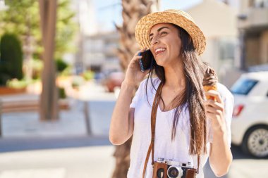 Genç İspanyol kadın turist akıllı telefondan konuşuyor ve sokakta dondurma yiyor.