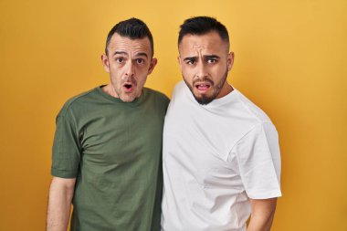Sarı arka planda duran eşcinsel çift, şaşkın, şüpheci ve alaycı görünüyorlar, ağzı açık kalınca şaşırıyorlar. 