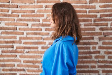 Güzel esmer kadın tuğla duvarın üzerinde duruyor, yan bakıyor, rahat profil pozu veriyor, doğal bir yüzü ve kendine güvenen bir gülümsemesi var.. 