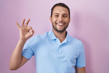 Pembe arka planda duran İspanyol adam gülümsüyor ve el ve parmaklarıyla 