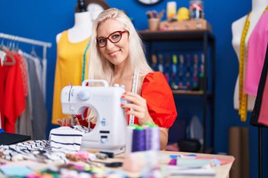 Dikiş atölyesinde dikiş makinesi kullanan kendine güvenen genç sarışın kadın terzi.