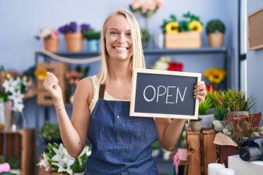 Çiçekçide çalışan beyaz bir kadın gururla haykırıyor, zaferi kutluyor ve kollarını kaldırıp başarıyı kutluyor. 