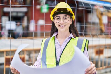 Young hispanic woman architect reading plans at street