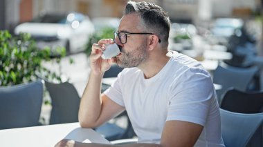 Kahve içen gri saçlı adam kahve dükkanının terasında oturuyor.