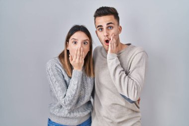Beyaz arka planda duran genç İspanyol çift korkmuş ve şok olmuş, şaşırmış ve şaşırmış bir halde. 