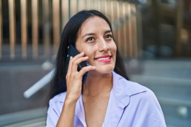 Genç, güzel, İspanyol bir kadın gülümsüyor ve caddede akıllı telefondan konuşuyor.