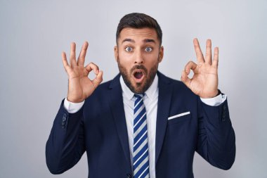 Yakışıklı, takım elbiseli ve kravatlı adam. Şaşırmış ve şaşırmış görünüyor. Onaylama sembolünü parmaklarıyla yapıyor. çılgın ifade 