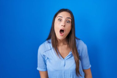 Mavi arka plan üzerinde duran genç esmer kadın şok olmuş yüz, şüpheci ve alaycı görünüyor, ağzı açık şaşırmış 