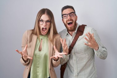 Beyaz arka planda duran genç çift çılgın ve kızgın bir şekilde bağırıyor ve agresif bir ifade ve kolla bağırıyor. hüsran kavramı. 