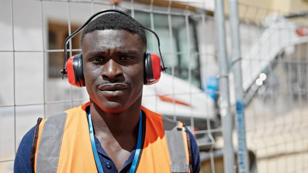 建筑工地上戴着严肃面孔的耳机的非裔美国人 — 图库照片