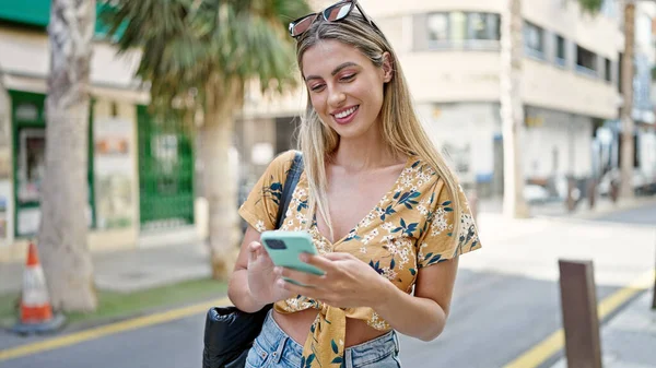 Sokakta akıllı telefon kullanan, kendine güvenen genç sarışın kadın.