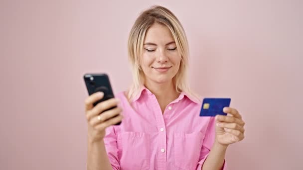 若いですブロンド女性ショッピングオンラインでスマートフォンやクレジットカードで隔離されたピンクの背景 — ストック動画