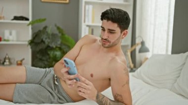 Latin asıllı genç bir adam yatak odasındaki yatakta video görüşmesi yapıyor.