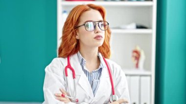 Genç, kızıl saçlı, gözlüklü kadın klinikteki masada oturuyor.