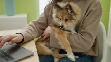 Yemek odasında laptopunu kullanan köpekli genç İspanyol kadın.