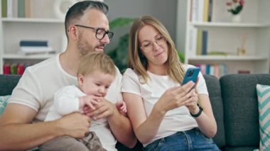 Anne, baba ve bebeğin ailesi evdeki kanepede selfie çekiyor.