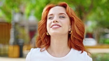 Parkta kendinden emin gülümseyen genç kızıl saçlı kadın.