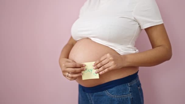 Молодая Беременная Женщина Кладет Мальчика Напоминание Бумаге Животе Изолированный Розовый — стоковое видео
