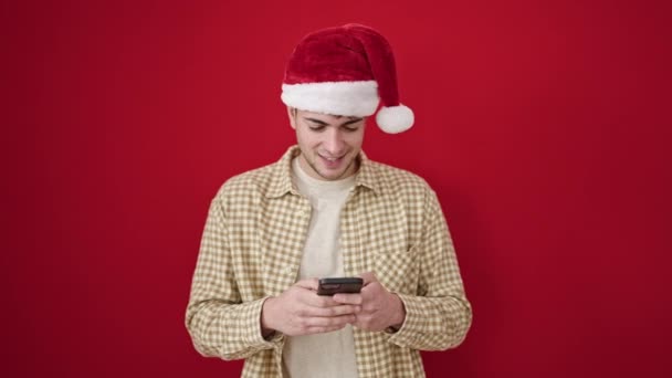 Junger Hispanischer Mann Mit Weihnachtsmütze Feiert Mit Smartphone Vor Isoliertem — Stockvideo