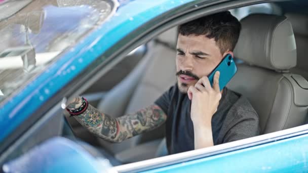 スマートフォンで話す若いヒスパニックの男 通りで祝う車に座って — ストック動画
