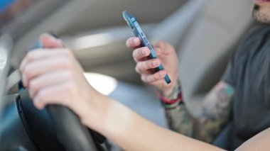 Young hispanic man using smartphone sitting on car at street
