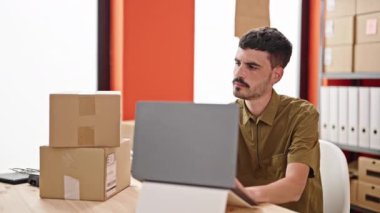 Genç Hispanik iş adamı ofisteki dizüstü bilgisayarla paketleri kontrol ediyor.